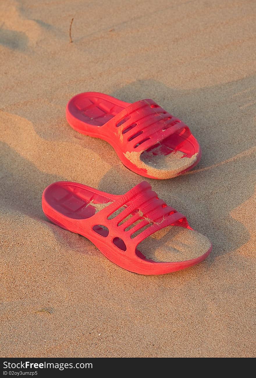 Red rubber beach shoes on the sand background. Red rubber beach shoes on the sand background