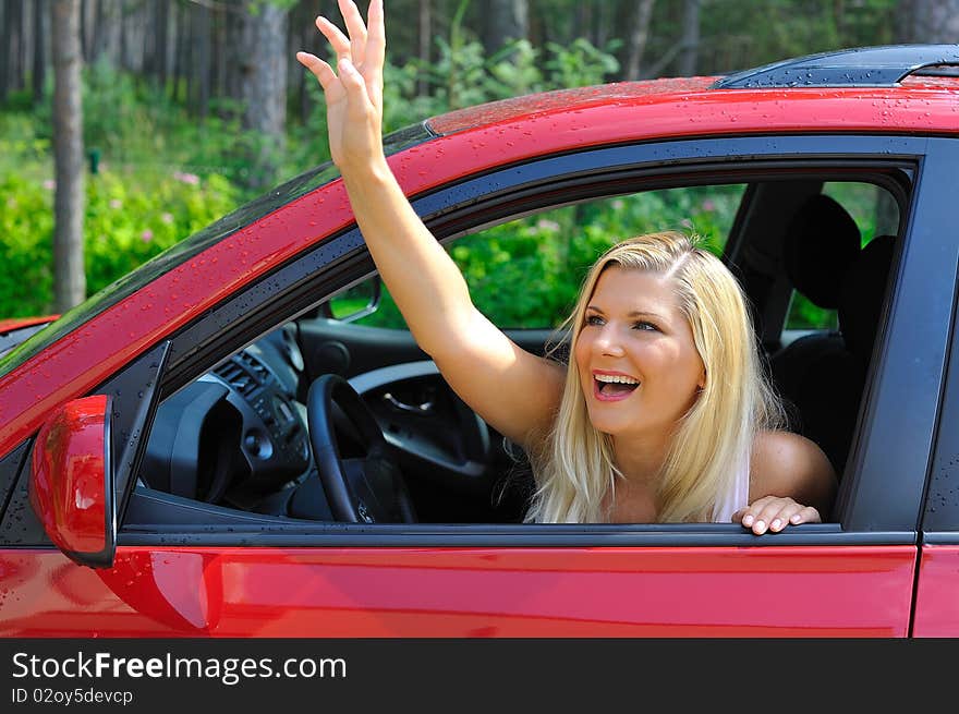 Beautiful woman driver in red shiny car outdoors smiling and waving with hand