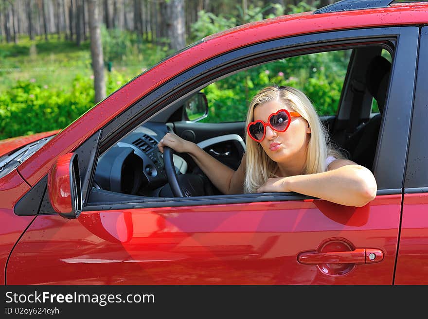 Beautiful funny woman in heart shaped glasses in red shiny car outdoors. Beautiful funny woman in heart shaped glasses in red shiny car outdoors