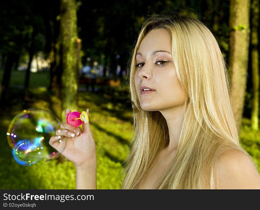 Blonde young woman blowing soap bubbles in summer day. Blonde young woman blowing soap bubbles in summer day