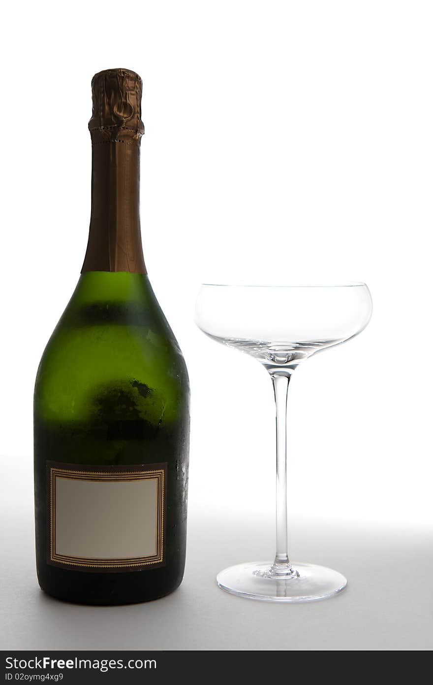 An unopened green bottle of champagne (with a blank label) next to an empty saucer style champagne glass.  Studio isolated on a white background. An unopened green bottle of champagne (with a blank label) next to an empty saucer style champagne glass.  Studio isolated on a white background.