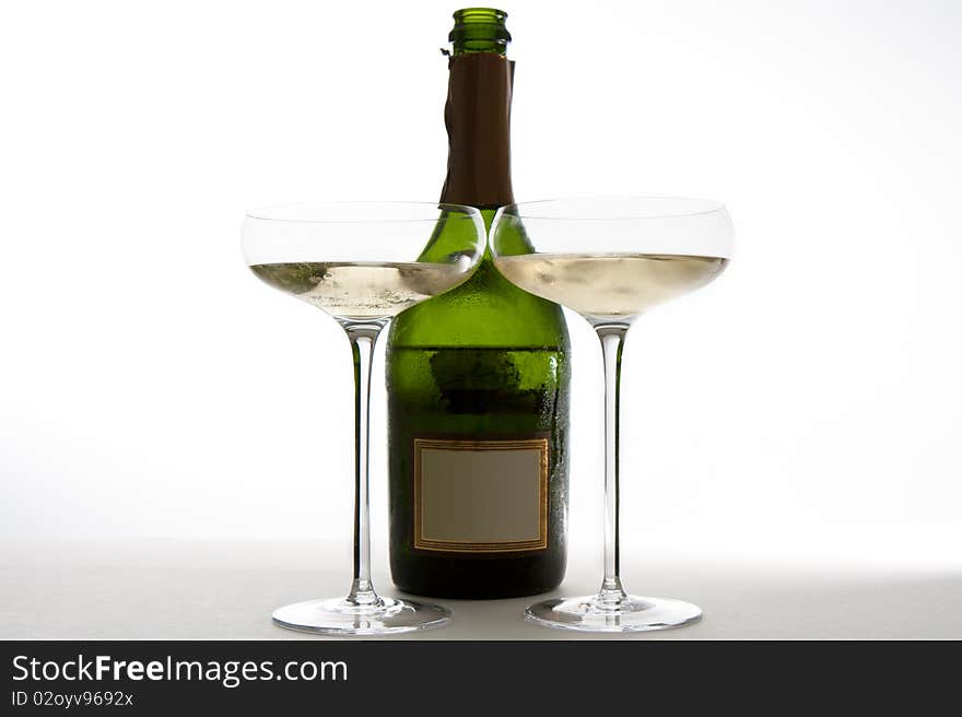 Two saucer style champagne glasses full of champagne next to a green bottle of champagne (opened).  The label has been blanked. Two saucer style champagne glasses full of champagne next to a green bottle of champagne (opened).  The label has been blanked.