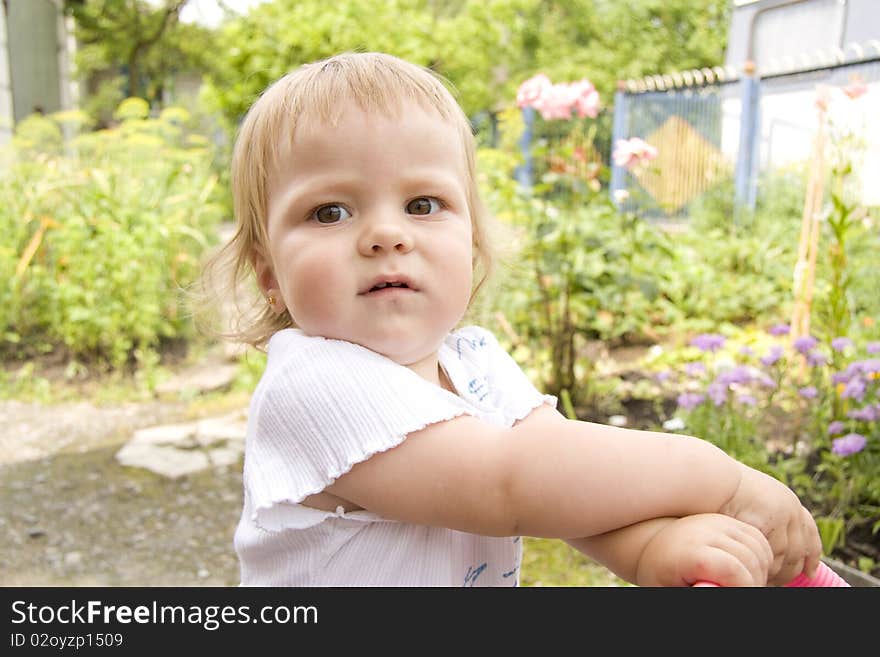 The small child walks with a children's carriage in the summer in a garden and distracts. The small child walks with a children's carriage in the summer in a garden and distracts