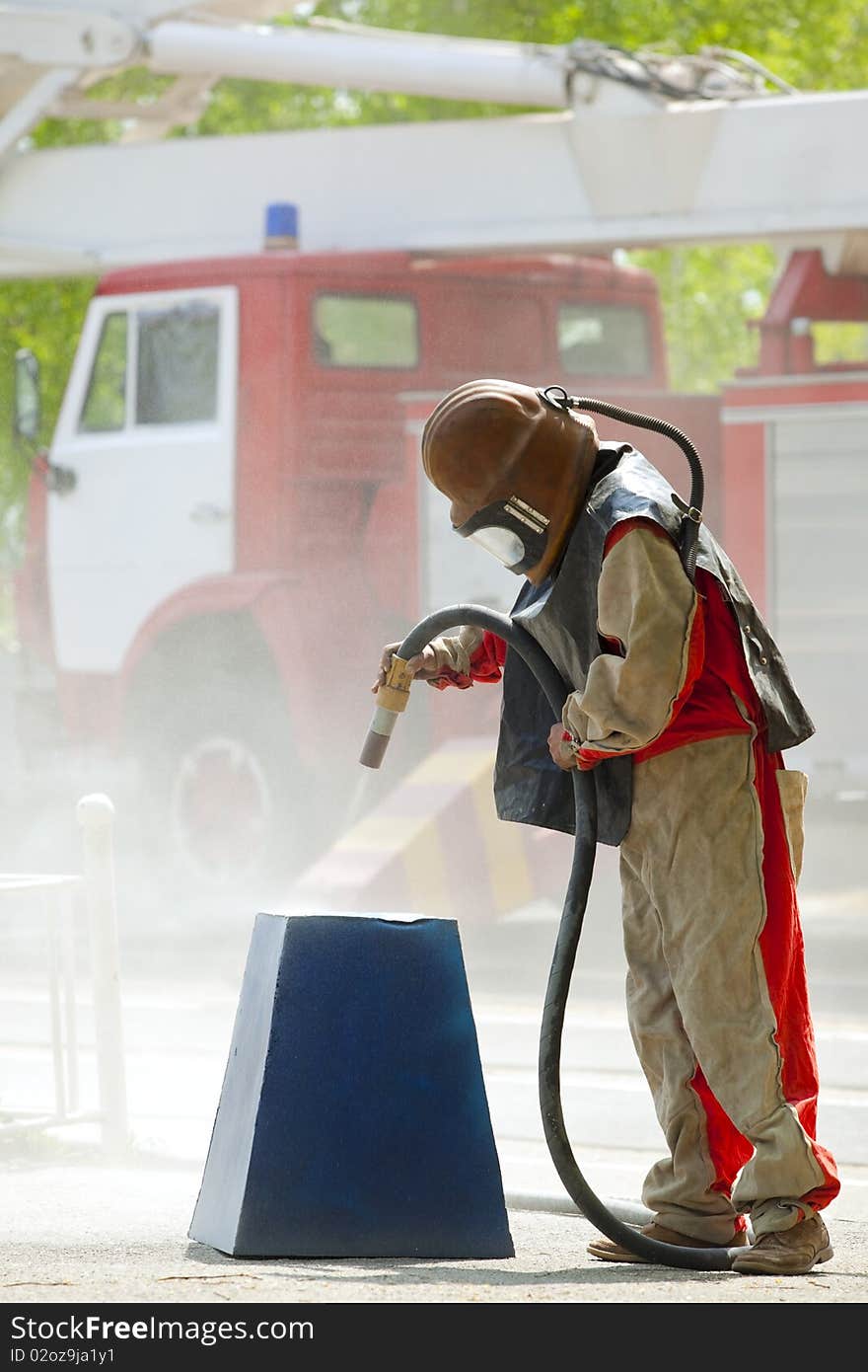 Worker in a protective suit spraying sand with abrasive peeler