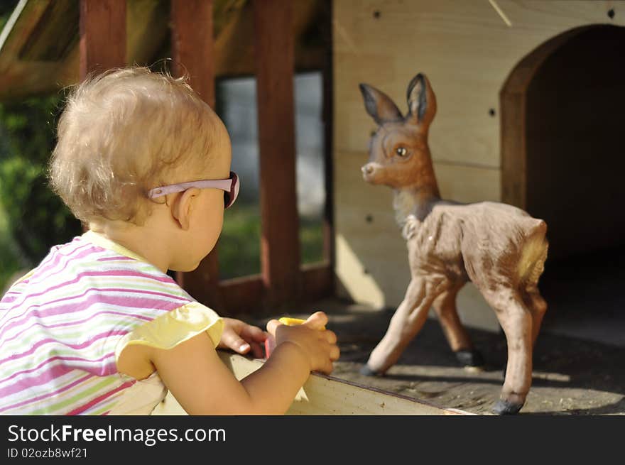 Sweet little baby girl is looking on sweet little roe-deer. Sweet little baby girl is looking on sweet little roe-deer