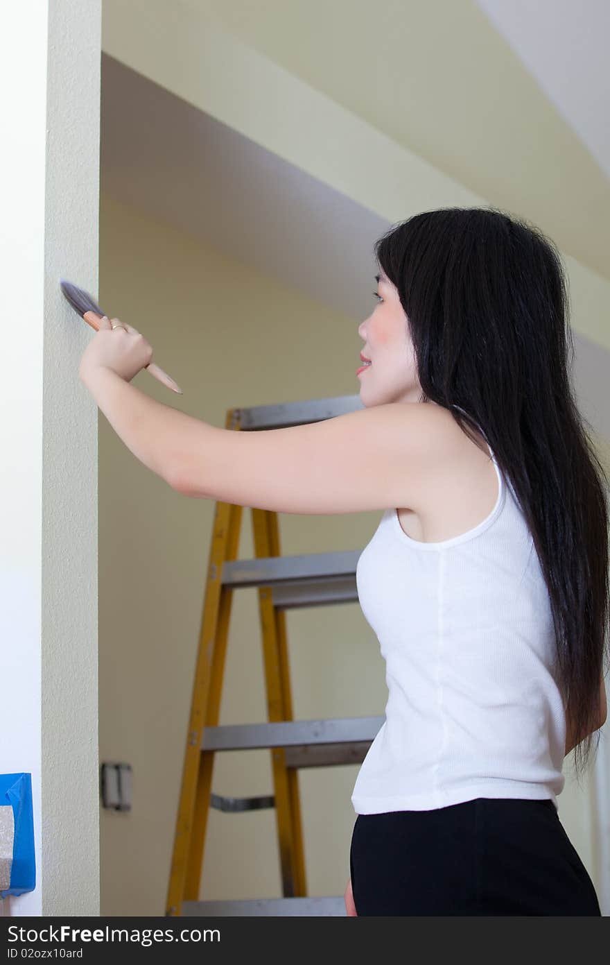 Asian Woman Contractor painting wall with ladder in background.