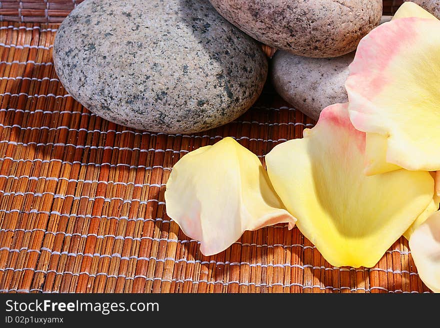 Yellow with a pink shade petals of roses on a wooden laying together with stones for salon SPA.