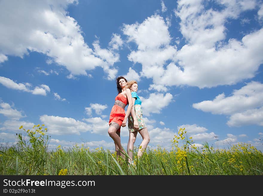 Two beautiful young women standing back to back on summer field enjoying wind wave. Two beautiful young women standing back to back on summer field enjoying wind wave