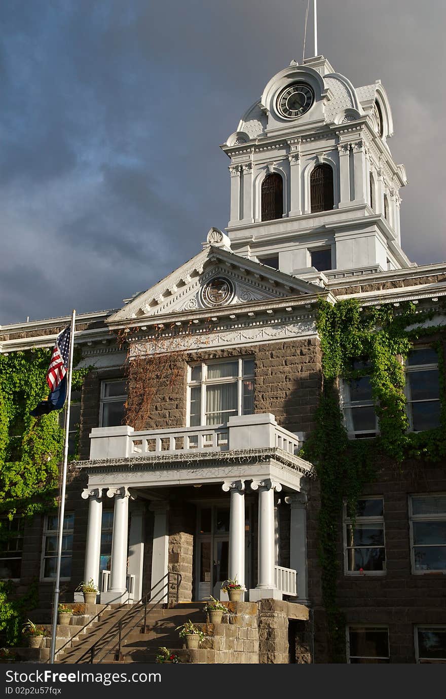 An American flag flies before the county courthouse in Prineville, Oregon, lit by the setting sun, against the background of a stormy sky. An American flag flies before the county courthouse in Prineville, Oregon, lit by the setting sun, against the background of a stormy sky