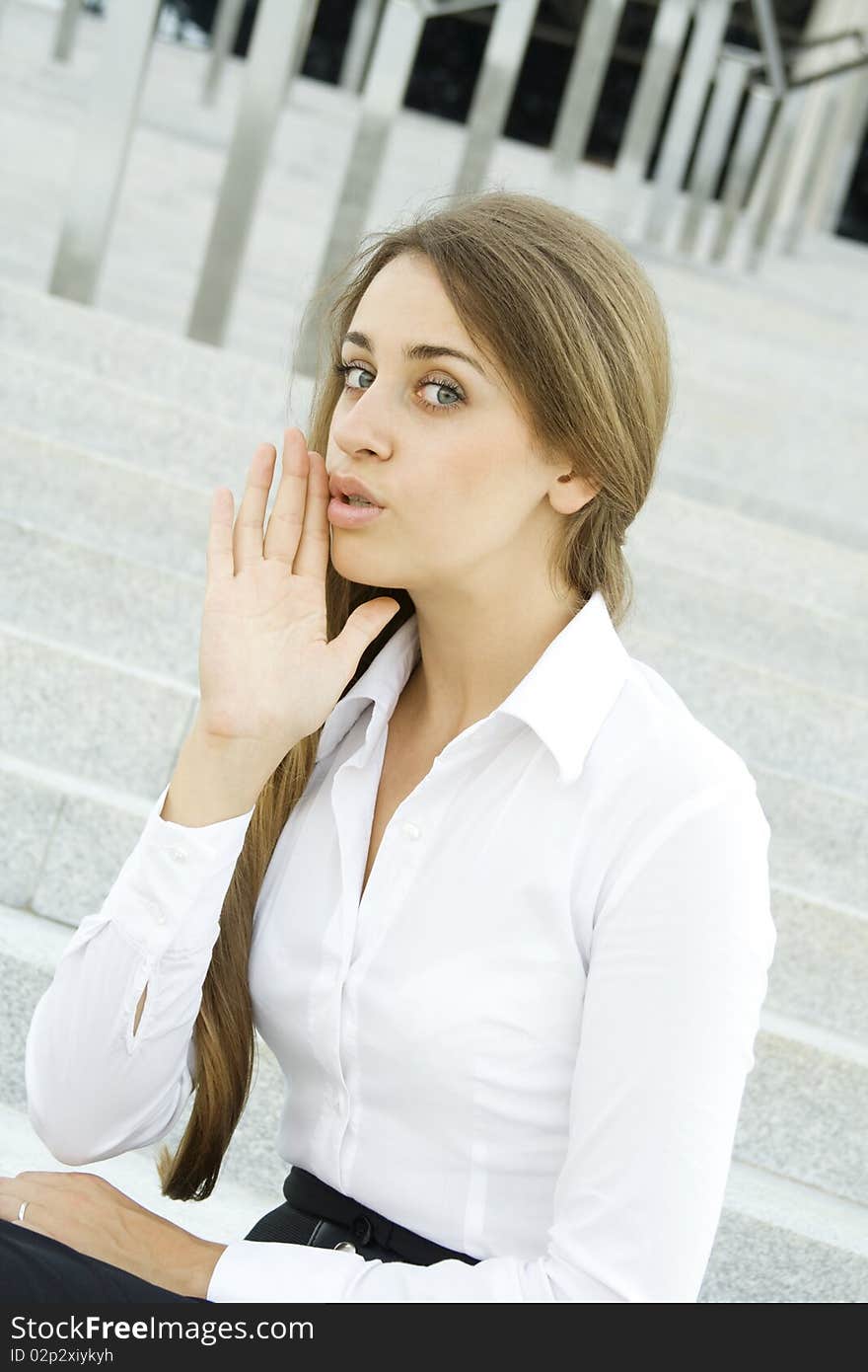 Young business woman on the background of stairs office building whispers trade secrets. Young business woman on the background of stairs office building whispers trade secrets