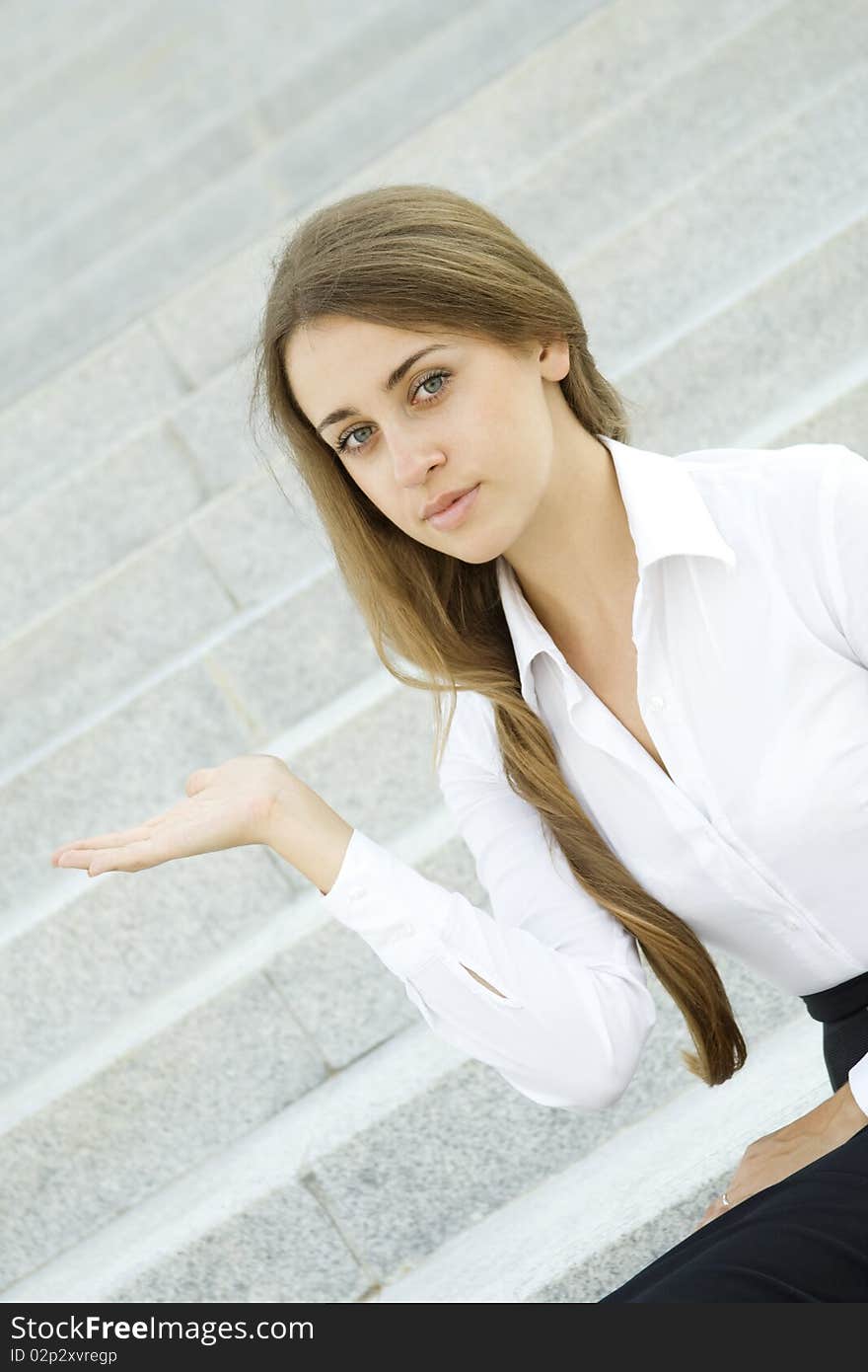 Businesswoman gesturing. Young business woman on a background of office building showing stairs. Businesswoman gesturing. Young business woman on a background of office building showing stairs