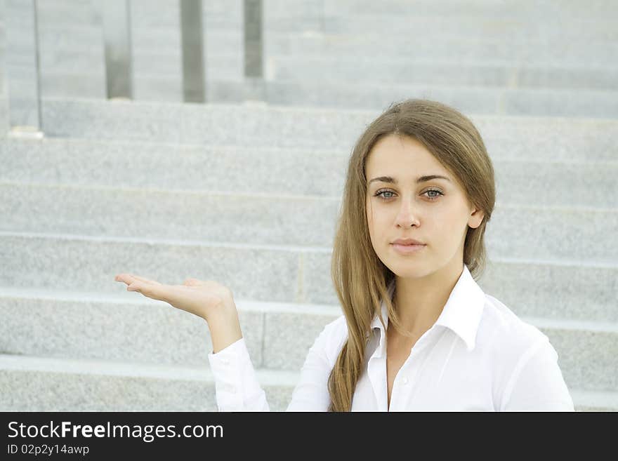 Businesswoman gesturing. Young business woman on a background of office building showing stairs. Businesswoman gesturing. Young business woman on a background of office building showing stairs