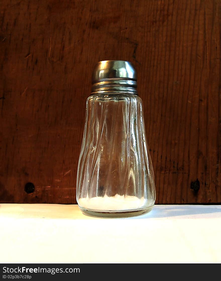 Almost empty salt shaker in front of wooden background