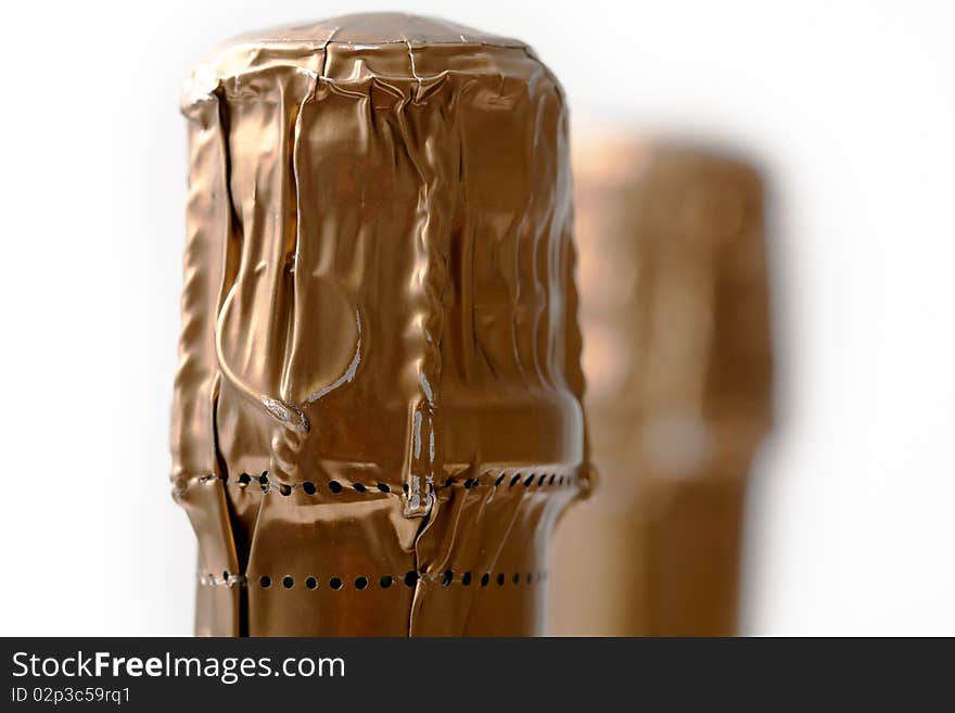 A macro shot of the very top of a champagne bottle showing the wire underneath the gold foil.  Two bottles with shallow DOF, focus on the front bottle. A macro shot of the very top of a champagne bottle showing the wire underneath the gold foil.  Two bottles with shallow DOF, focus on the front bottle.