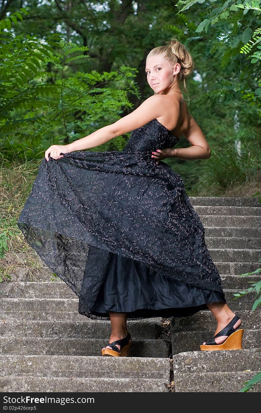 Beautiful young lady standing on old staircase somewhere in green park. Beautiful young lady standing on old staircase somewhere in green park