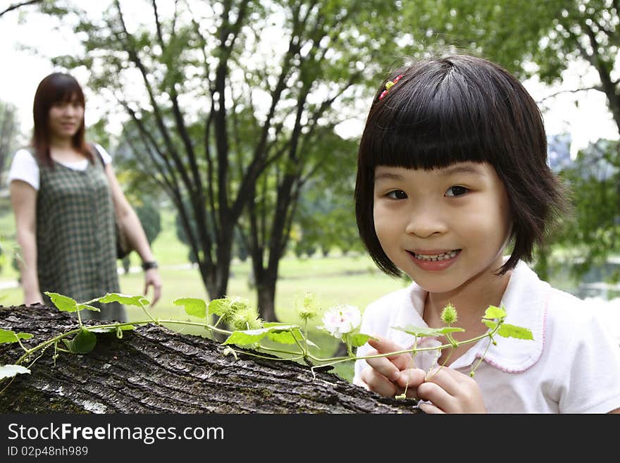 A curious Asian girl examining a creeper plant as her mother watches. A curious Asian girl examining a creeper plant as her mother watches