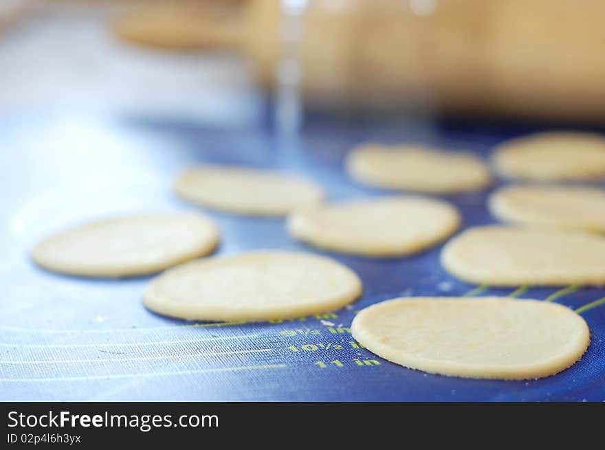 Rolled dough with round dough slices on a blue pastry board, standing next to a glass and rolling pin.