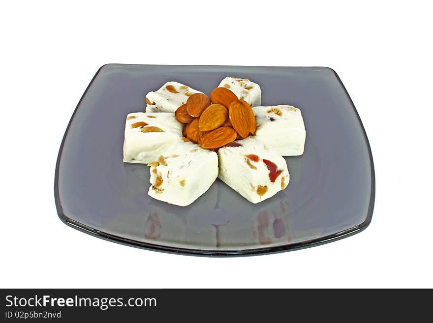 Delicious nougat with almonds on black glass plate, isolated on white