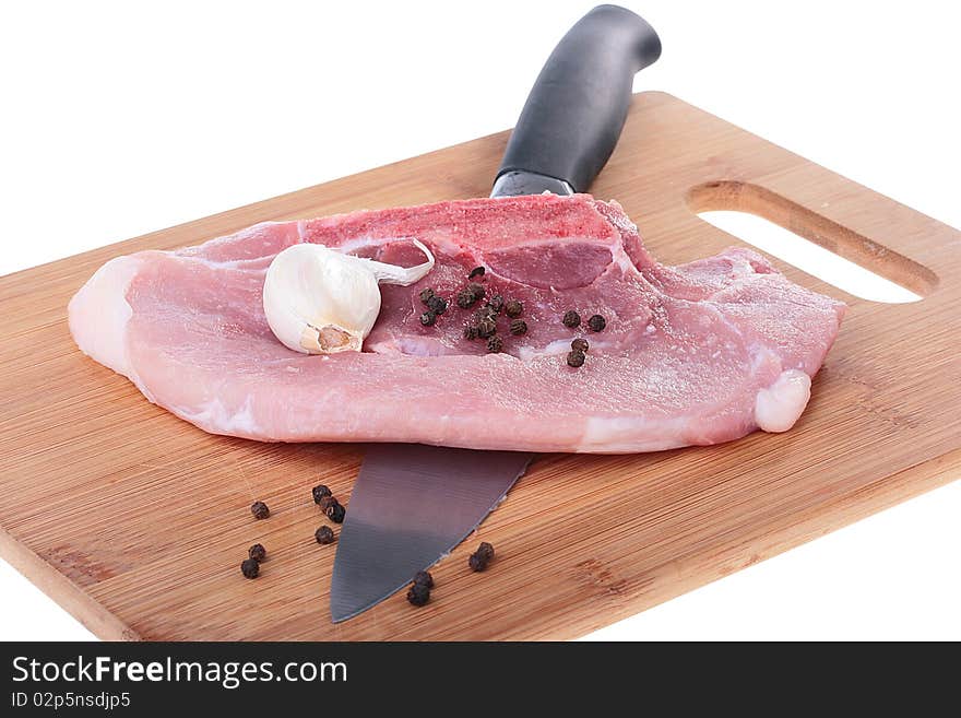 Piece of crude meat with black pepper and garlic on a kitchen board. Piece of crude meat with black pepper and garlic on a kitchen board.