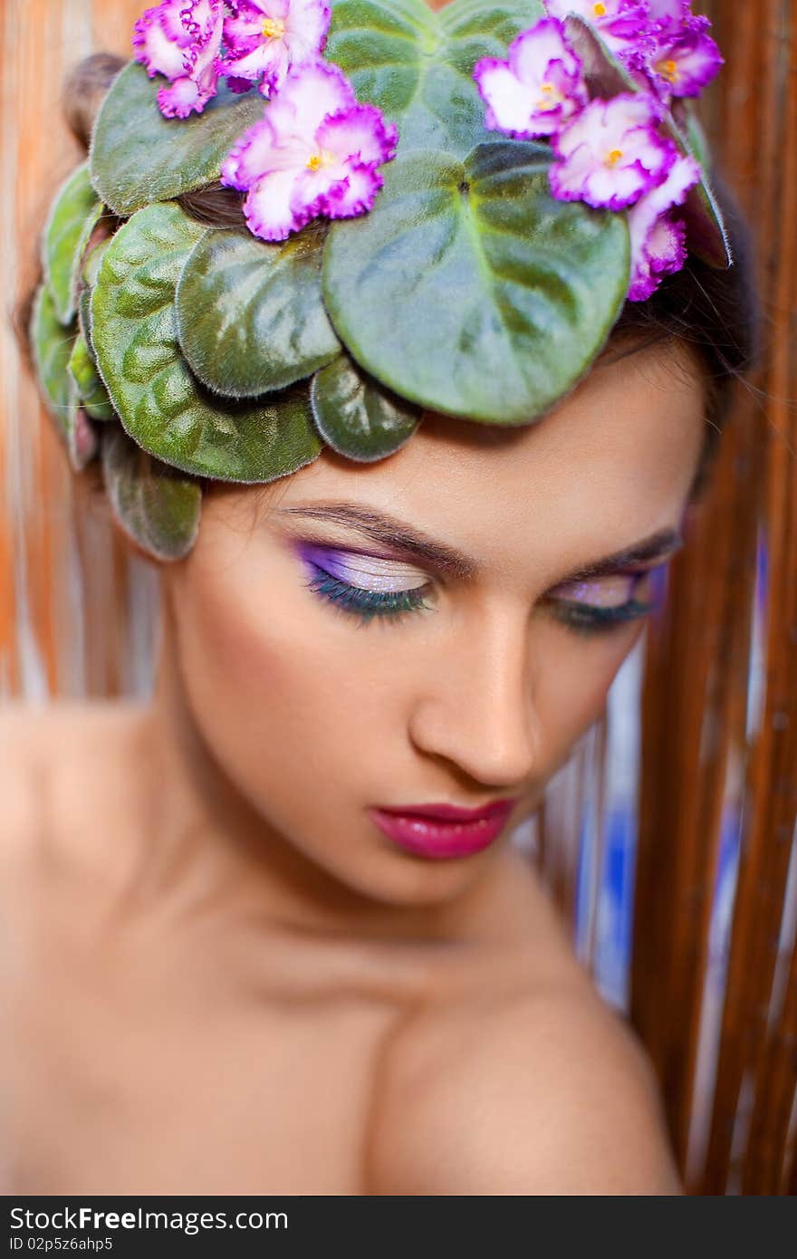 Beautiful girl with a wreath of flowers on her head on the background of bamboo fence