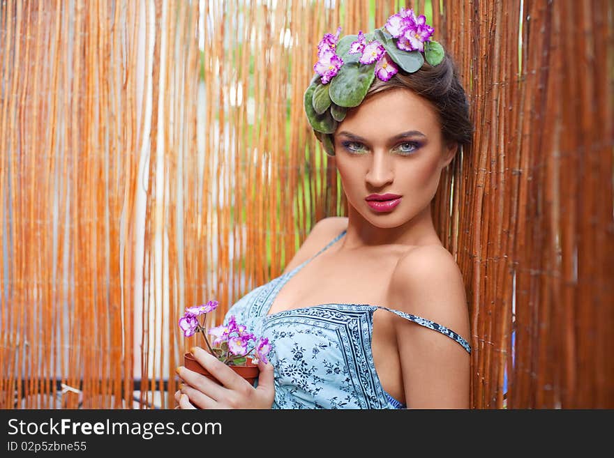 Beautiful girl with a wreath of flowers on her head on the background of bamboo fence