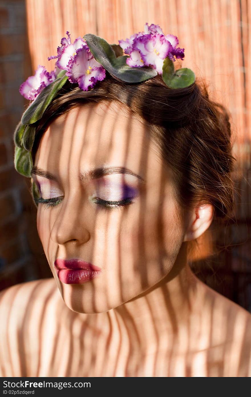 Beautiful girl with a wreath of flowers on her head on the background of bamboo fence