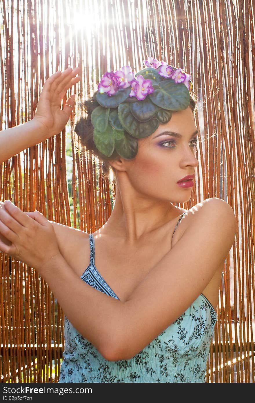 Beautiful girl with a wreath of flowers on her head on the background of bamboo fence