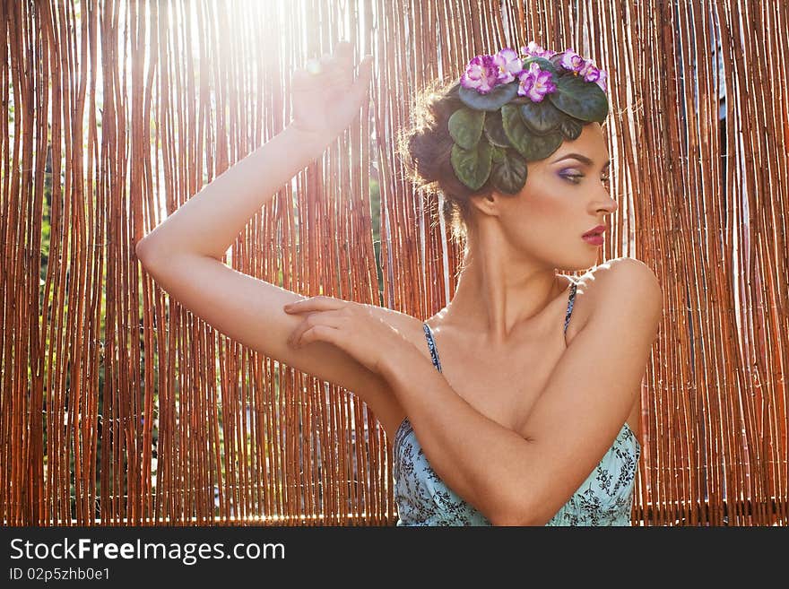 Beautiful girl with a wreath of flowers on her head on the background of bamboo fence