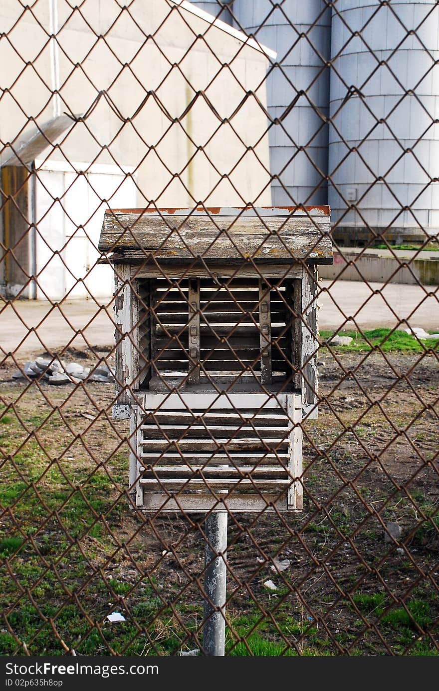 Decorative birdhouse made of tree and mounted on a piece of wood behind a chain link fence. Decorative birdhouse made of tree and mounted on a piece of wood behind a chain link fence.