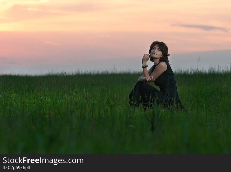 Photo of a young beautiful woman in a green wheat field at sunset. Photo of a young beautiful woman in a green wheat field at sunset