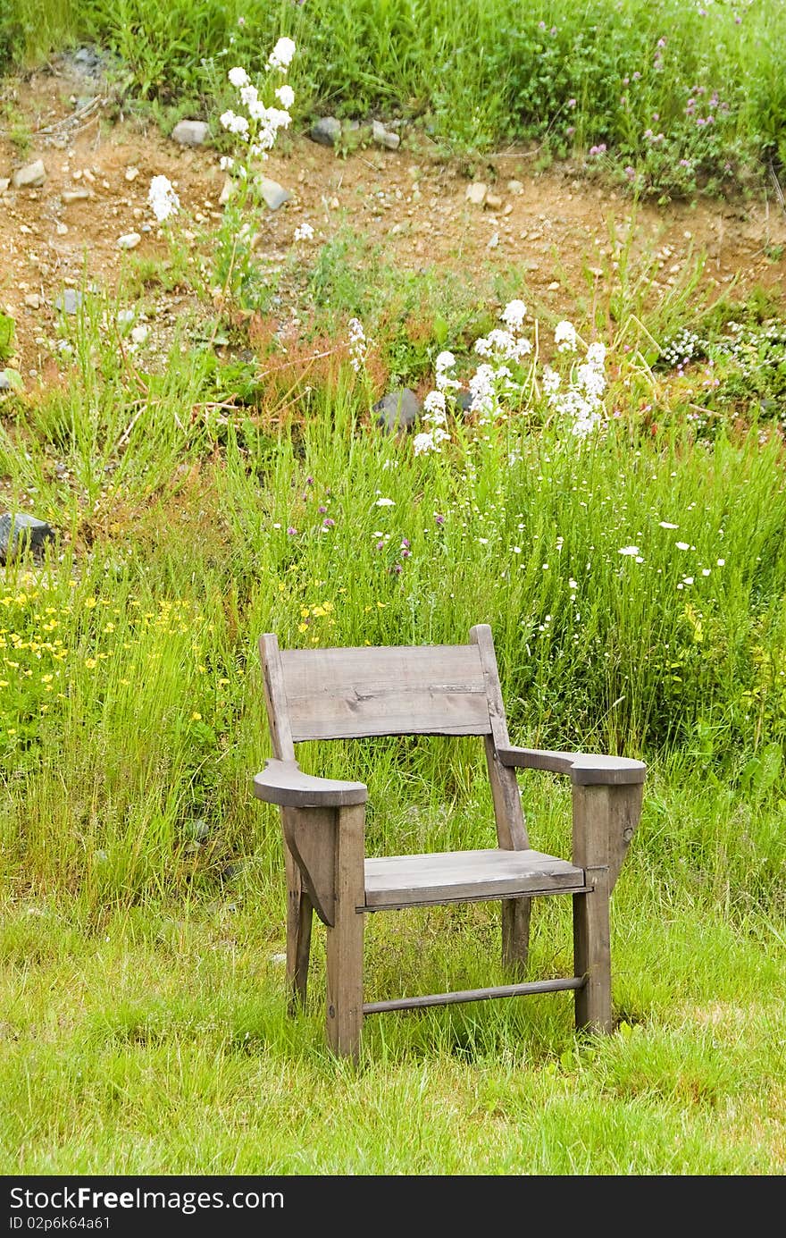 A wooden chair in front of a hill with grass and wild flowers.