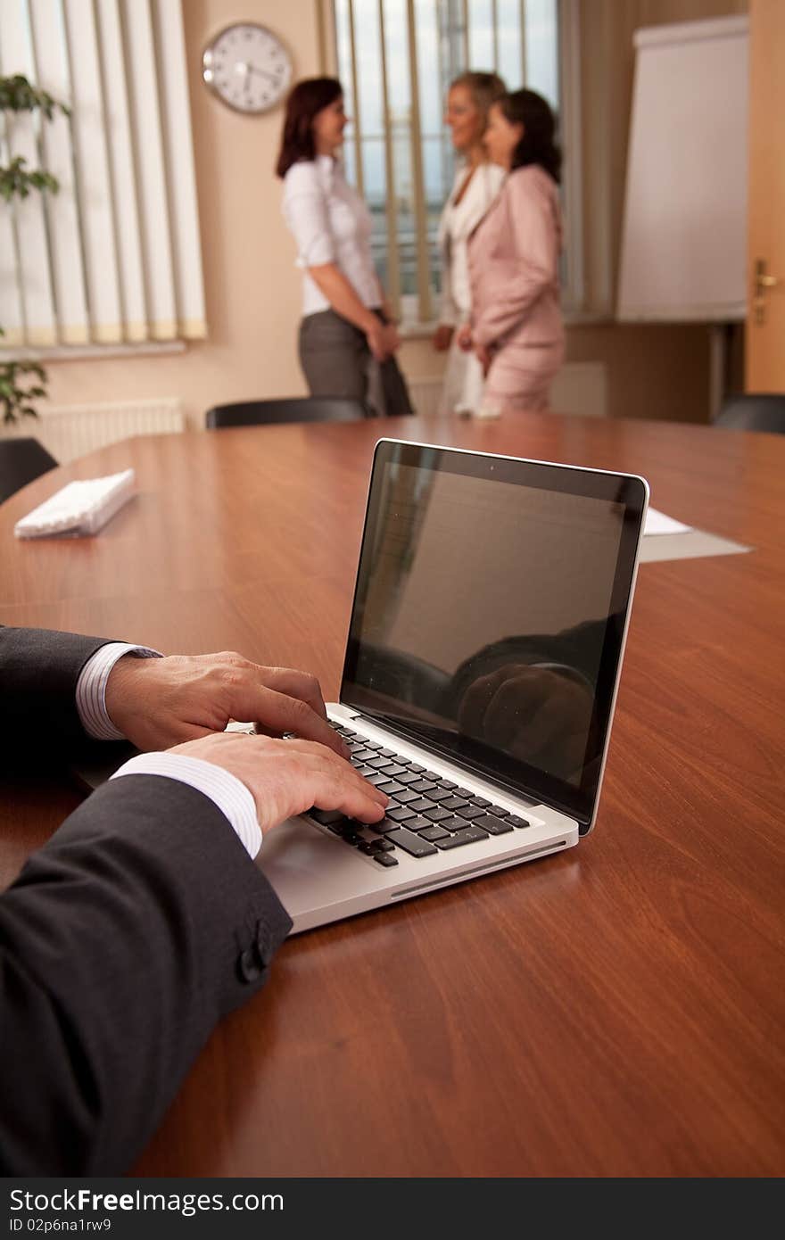 Businessman working on laptop, women talking in the background. Businessman working on laptop, women talking in the background