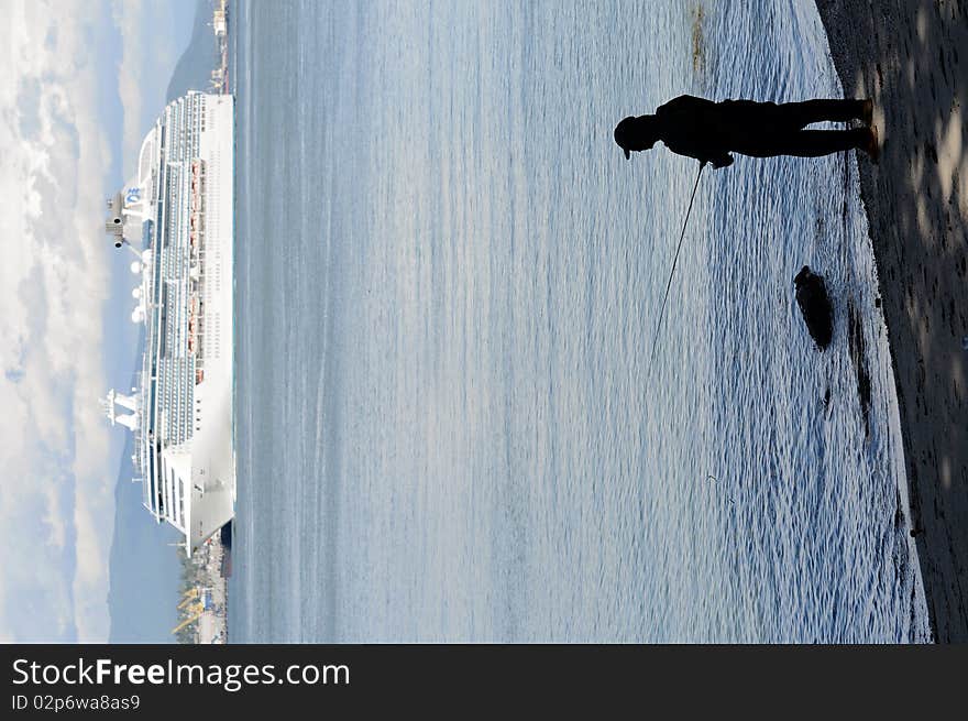 Man Fishing While A Ship Cruises By