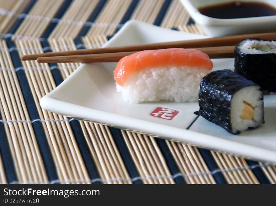 Small sushi on a plate with wood chopsticks on a rectangular decorated plate, on a wood table-cloth, close-up. Small sushi on a plate with wood chopsticks on a rectangular decorated plate, on a wood table-cloth, close-up