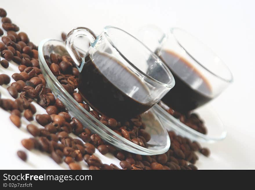 Two transparent glass coffee cups and some coffee beans on white background in diagonal. Two transparent glass coffee cups and some coffee beans on white background in diagonal