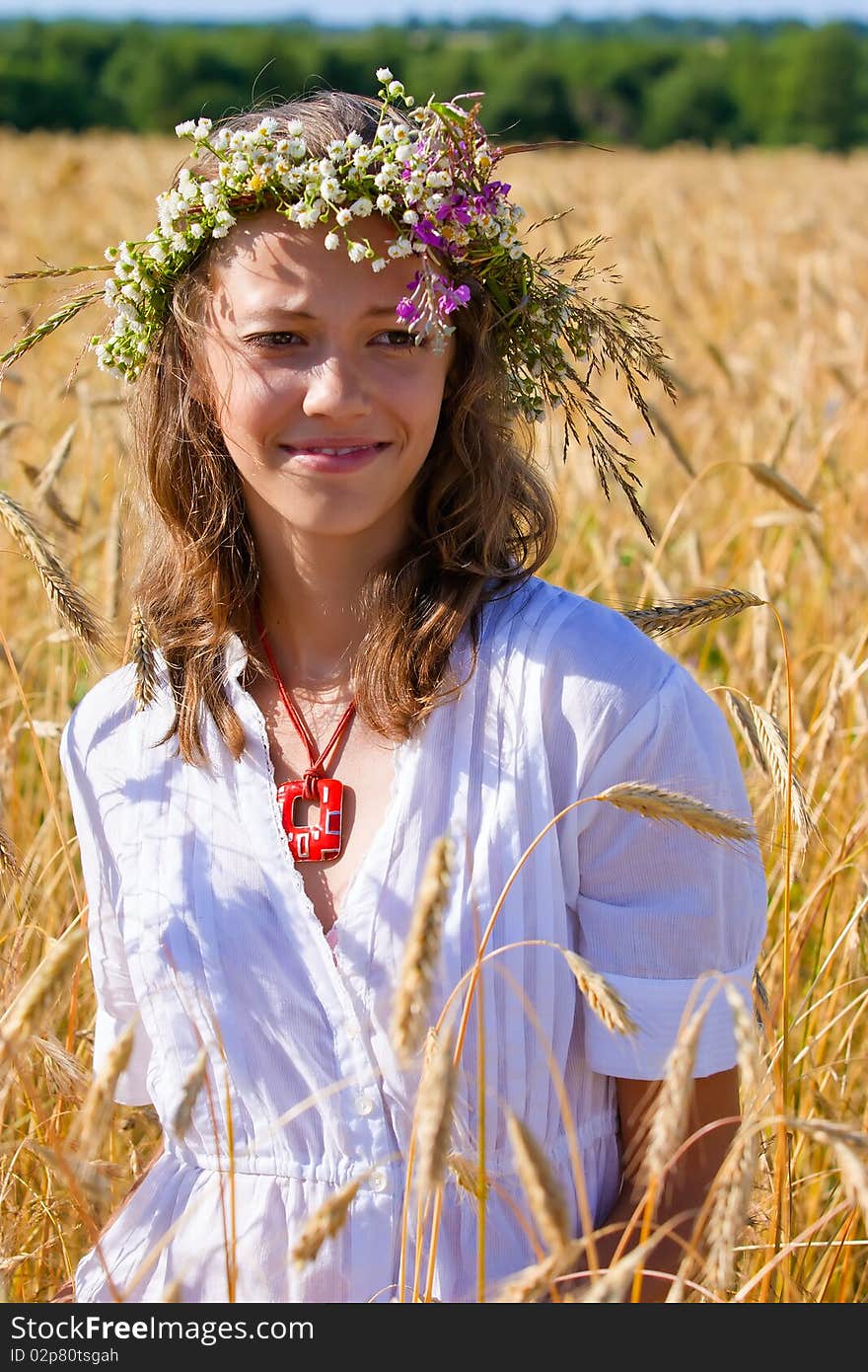 Russian girl in a wreath from camomiles is in a wheaten field