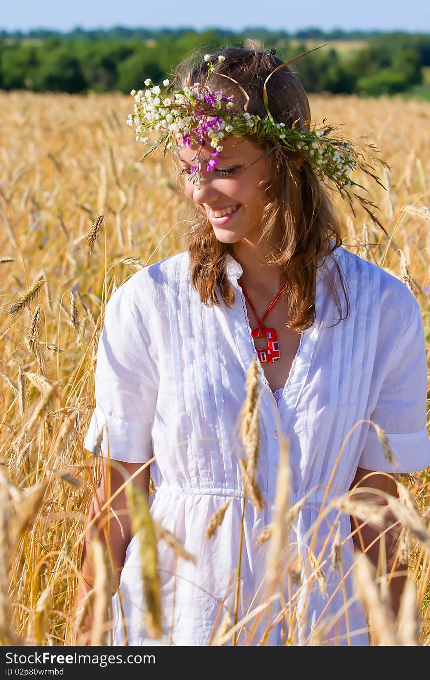 Russian girl in a wreath from camomiles is in a wheaten field