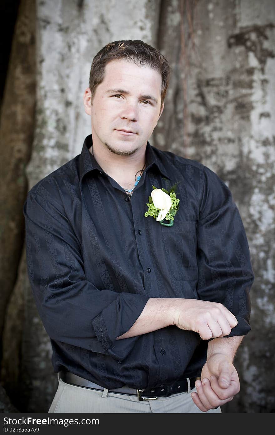 A half portrait of a handsome groom rolling up his shirt sleeves.