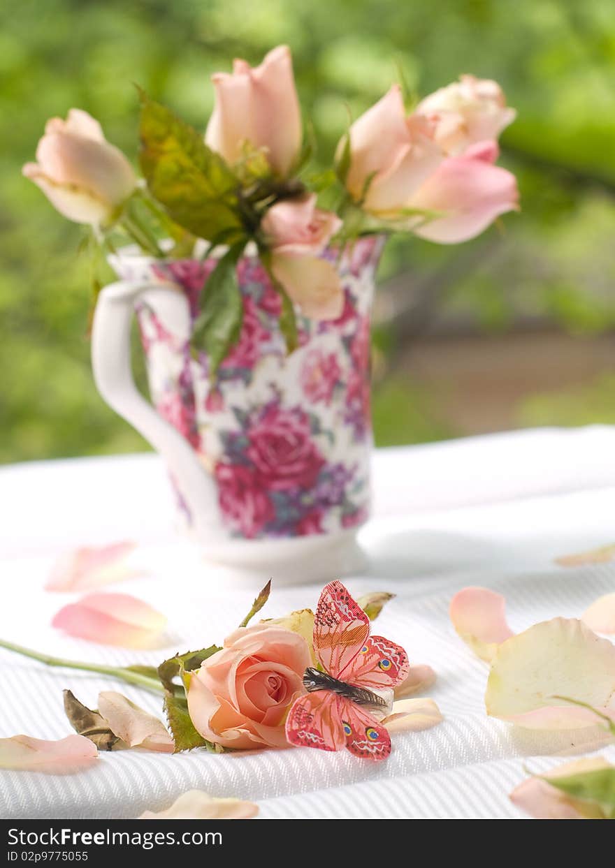 Rose and butterfly with roses in tea mug on background