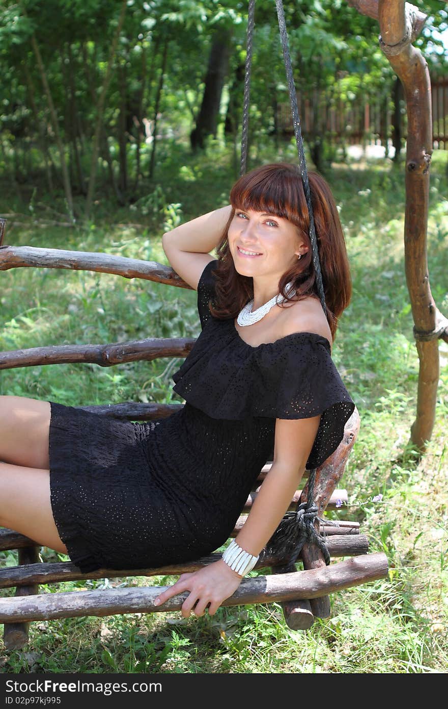 Happy brunette girl on the swing in the summer day