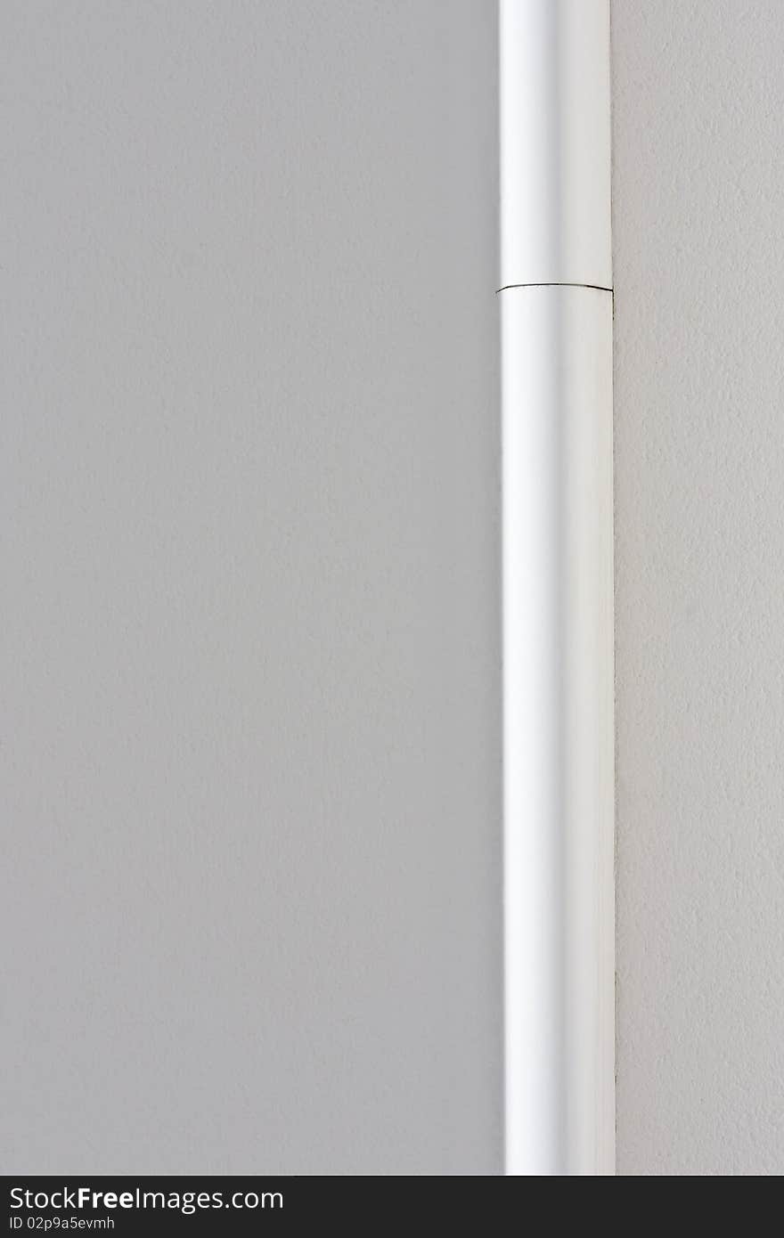 A white painted drainpipe on a white painted wall. A white painted drainpipe on a white painted wall