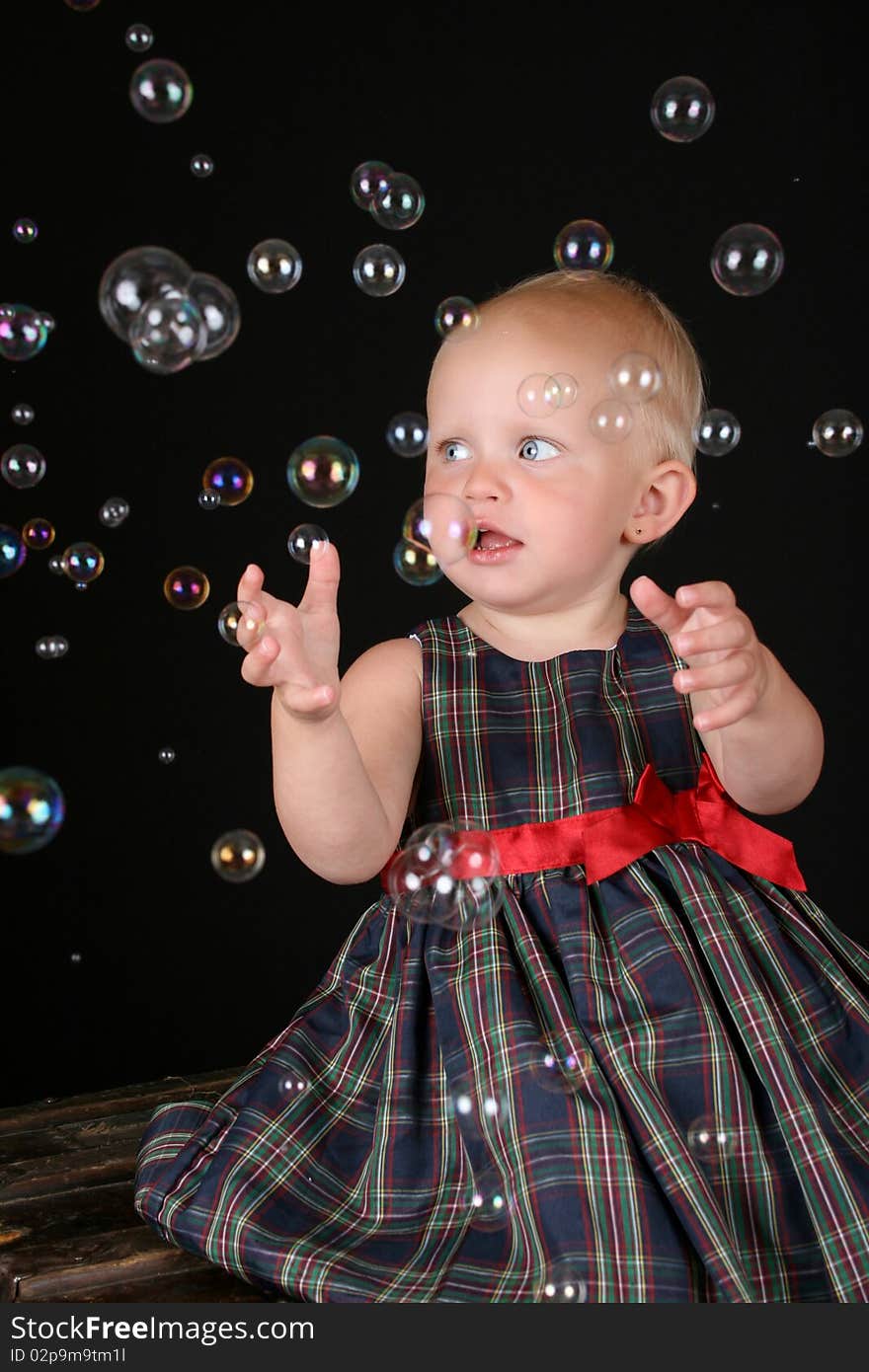 Cute blond toddler girl surrounded by bubbles sitting on a wooden trunk. Cute blond toddler girl surrounded by bubbles sitting on a wooden trunk