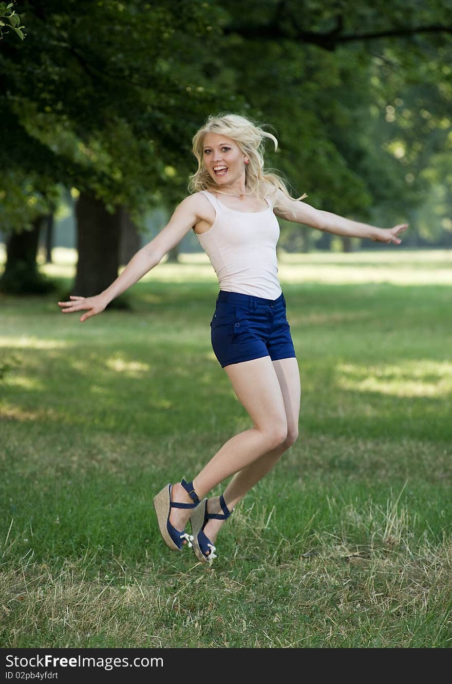 Young sportive blond jumps delighted under the trees in the park. Young sportive blond jumps delighted under the trees in the park