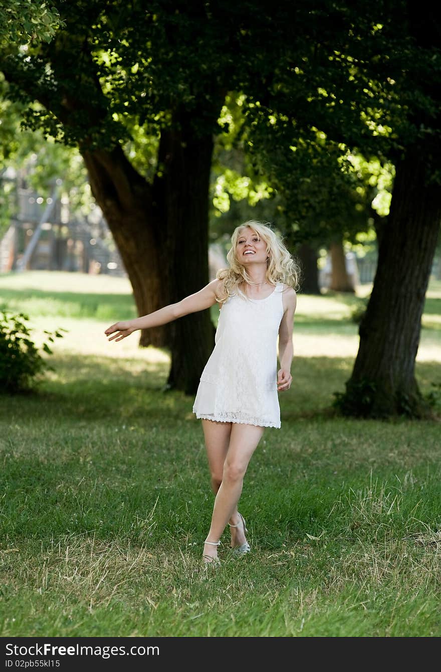 Young blond is dancing in her sundress under shadily trees in the park