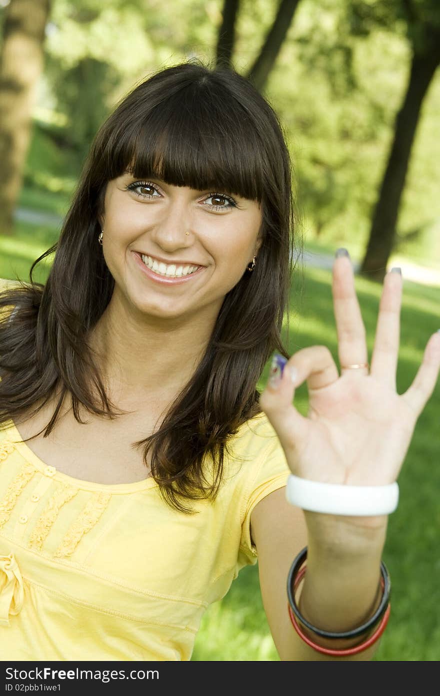 Young beautiful woman is smiling in a park and shows the sign OK