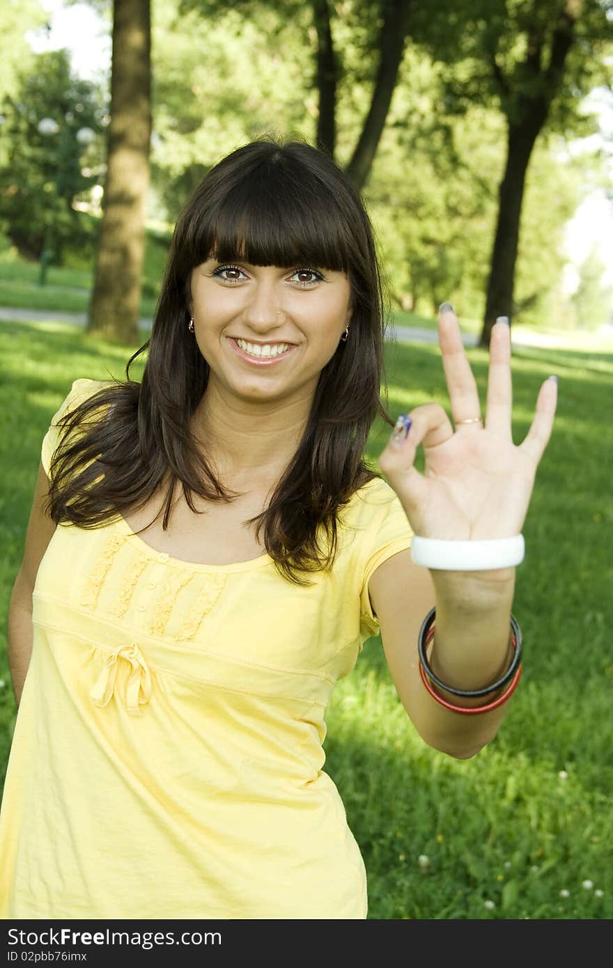 Young beautiful woman is smiling in a park and shows the sign OK