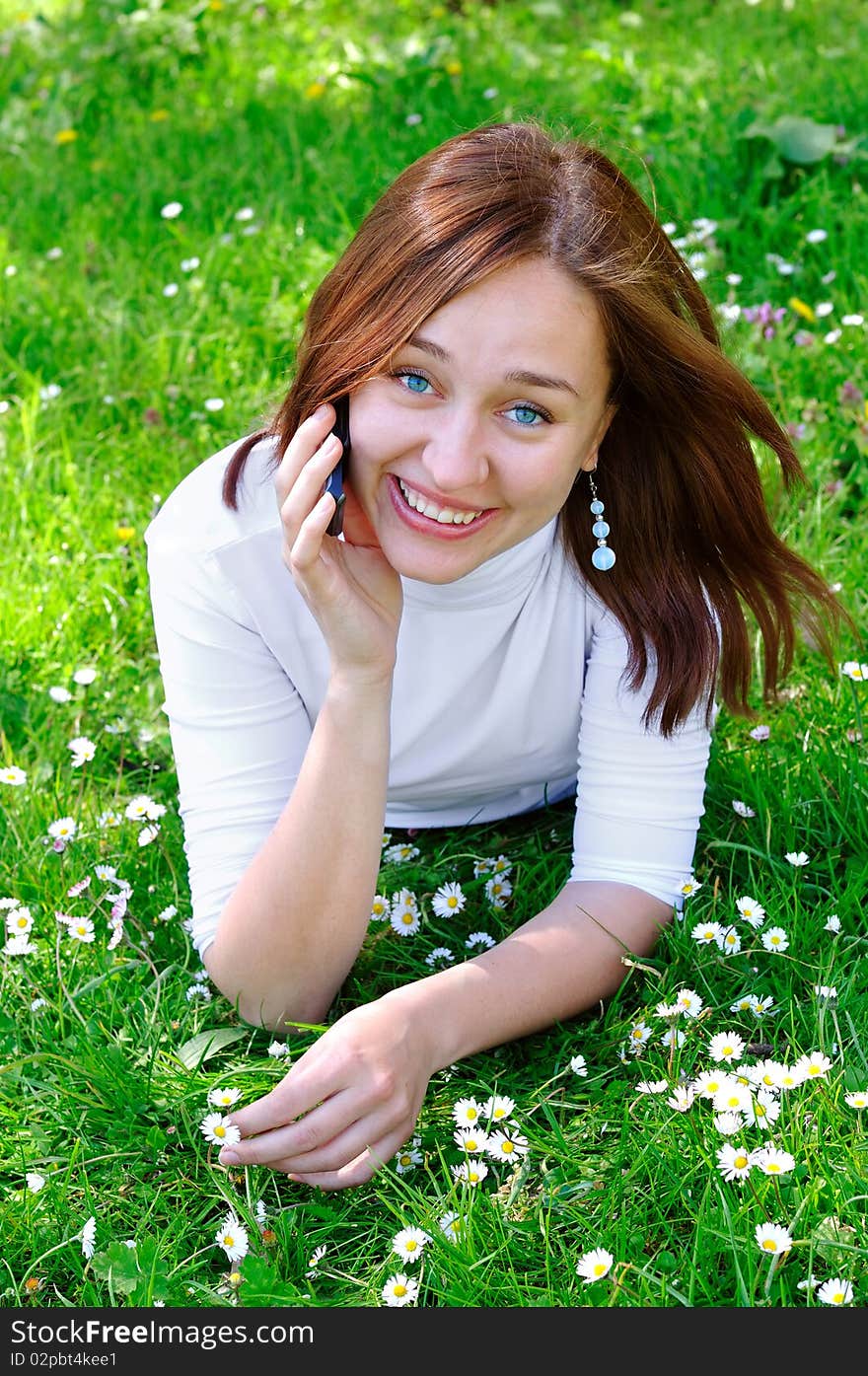 The girl with the phone on the grass, vertical