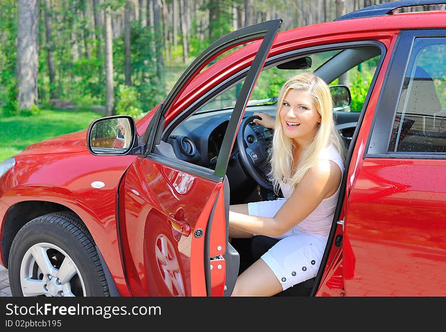 Beautiful woman driver in red shiny car opens the door