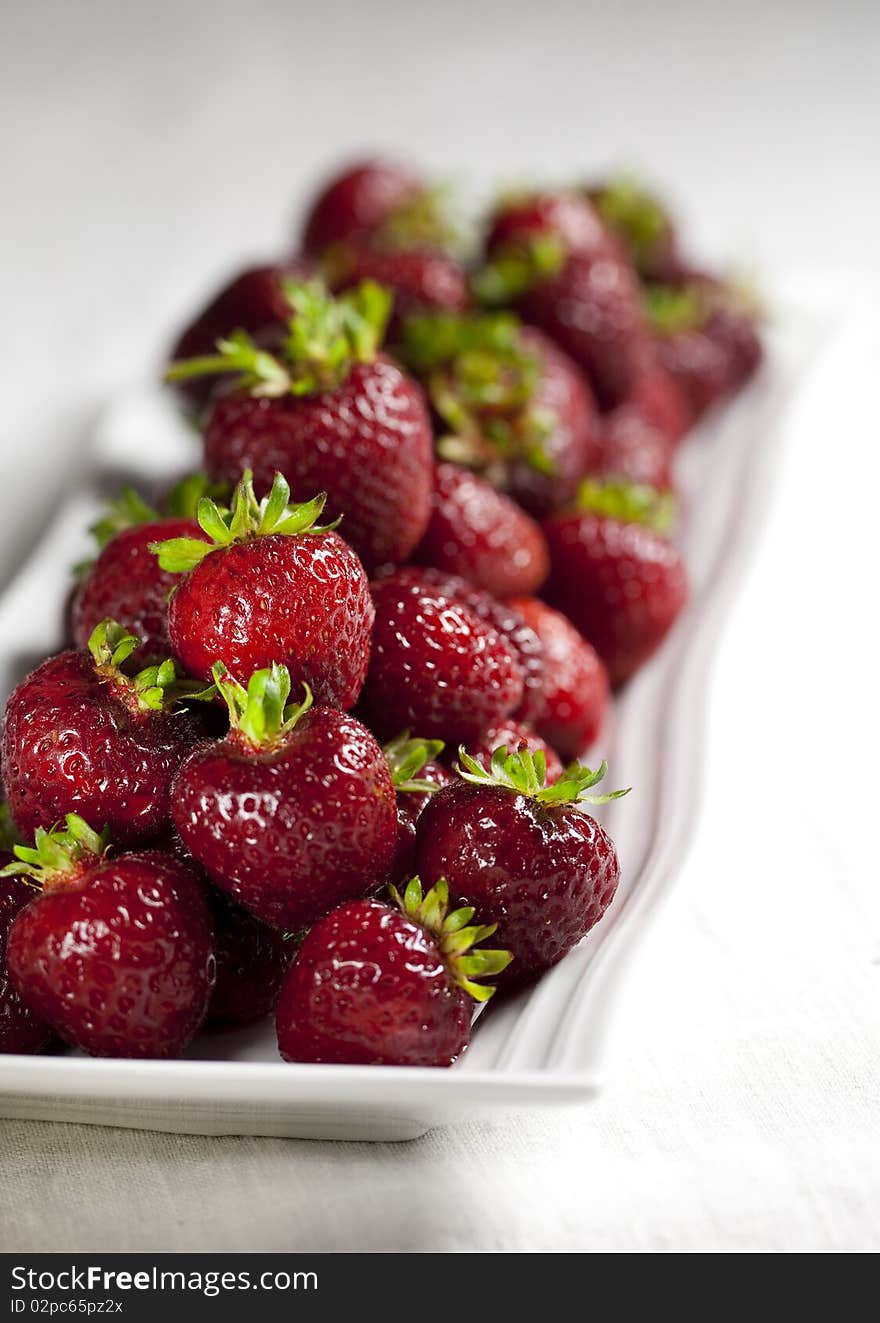 A long white platter filled with delicious strawberries. Shallow depth of field. A long white platter filled with delicious strawberries. Shallow depth of field.