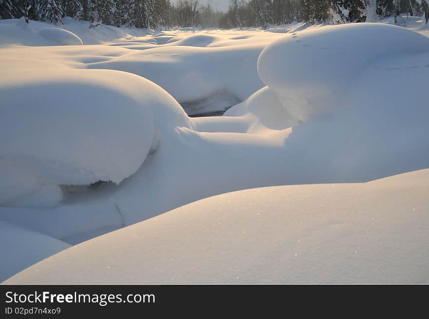 Thick fluffy snowdrifts on the mountain river bed in coloured sunset light. Thick fluffy snowdrifts on the mountain river bed in coloured sunset light.